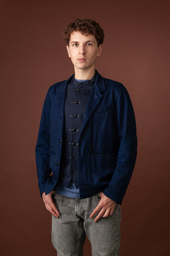 Studio portrait of a young white man in a blue jacket on a brown background