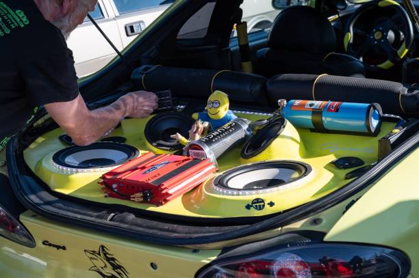 man working on a tuned yellow hyundai coupe with stereo and toys in the trunk - car stereo imagens e fotografias de stock