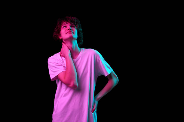 istock Charming young man looking up dreamily isolated over dark background in purple neon light. Positive emotions, youth, sales, ad 1435575099