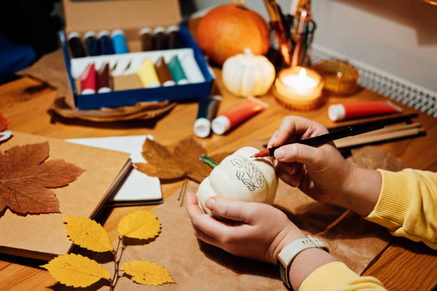 istock Autumn pumpkins craft. DIY Fall Crafts for Adults. Female hands draw patterns on white pumpkin against autumn decor background on the table at home 1435577811