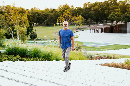Gray hair man walking, jogging and stretching in park in summer or autumn morning