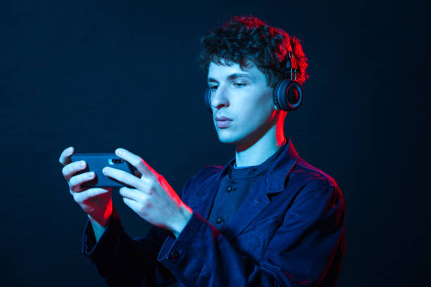 студийный портрет 24-летнего белого мужчины в беспроводных наушниках с мобильным телефоном - red blue white neon light стоковые фото и изображения
