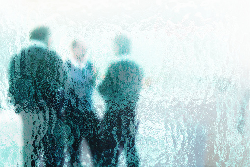 Men at a seminar standing and chatting, seen through rippled glass.