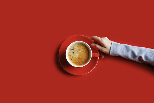 Woman's hand holding a cup of coffee on red background