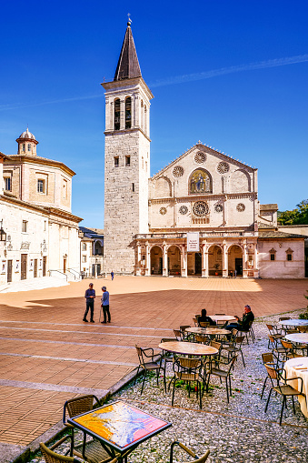 Spoleto, Umbria, Italy, October 20 -- A wide angle view of the beautiful Duomo, in the historic heart of the medieval city of Spoleto, in the Umbria region, central Italy. The Duomo, or Cattedrale di Santa Maria Assunta (Cathedral of Assumption of the Blessed Virgin Mary), was built starting from 1067 in Romanesque and Lombard style and consecrated in 1198. Spoleto was one of the major centers of the Umbrian people, before being conquered and becoming an important colony of Rome. In medieval times it was subjected to the dominion of the Lombards, becoming a Duchy. Spoleto, one of the most visited medieval cities in Italy, hosts the Festival of the Two Worlds, a world-famous event that brings together hundreds of artists, musicians, classical dancers and opera singers every year. The Umbria region, considered the green lung of Italy for its wooded mountains, is characterized by a perfect integration between nature and the presence of man, in a context of environmental sustainability and healthy life. In addition to its immense artistic and historical heritage, Umbria is famous for its food and wine production and for the quality of the olive oil produced in these lands. Super wide angle image in high definition format.