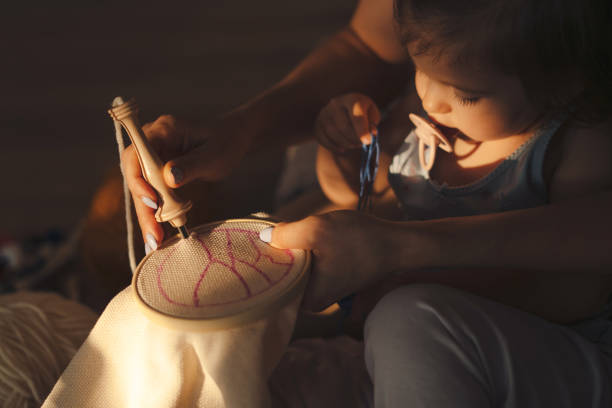 close-up de uma mãe mostrando sua filha bebê como desenhar o pano que ela vai bordar. retrato escuro. hobby e lazer criativos da família. mãe e filha adolescente juntos - embroider embroidery caucasian skill - fotografias e filmes do acervo