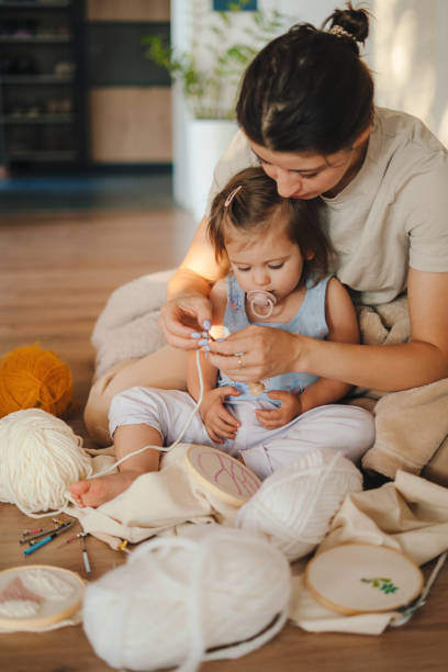 pleasant smart woman sitting together with her daughter teaching her to embroider. between generations. parent, child. creative design. - embroider imagens e fotografias de stock