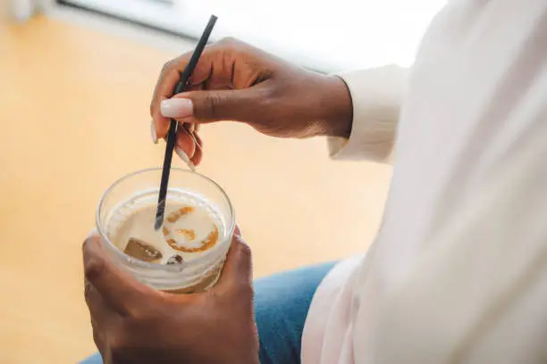 Portrait of woman's hands holding a glass of iced-coffee in a street cafe. LadyÂ is enjoying a cold drink alone. Businesswoman enjoys relaxing with glass of caffeine on coffee break for refreshment.