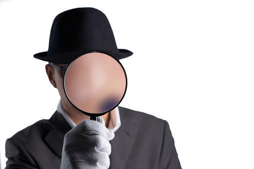 businessman with hat holding magnifying glass against white background