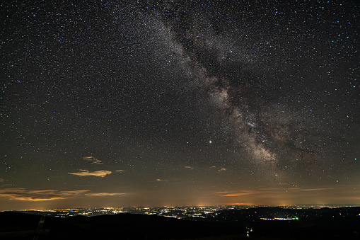 Many stars and milky way on night sky over illuminated city from high up on a hill