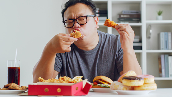 El hombre gordo asiático disfruta de comer comida chatarra poco saludable, hamburguesa, pizza, pollo frito photo