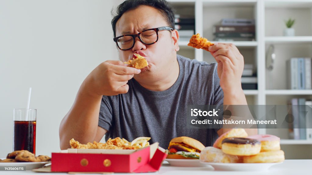 Asian fat man enjoy to eat unhealthy junk food, hamburger, pizza, fried chicken Eating Stock Photo