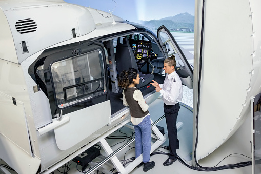 High angle view of male instructor giving a female student some guidance before start of training session in a helicopter flight simulator. Pilot talking to student and preparing her for a day of training in a flight simulator.