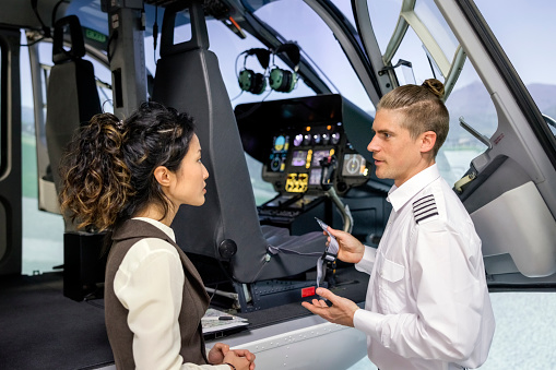 Pilot instructor talking with female student while standing outside helicopter simulator. Flight instructor giving instructions to a female student before a training session.