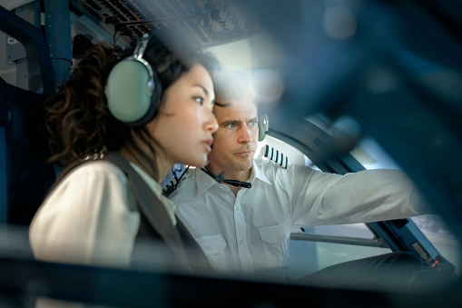 Pilot explaining how a flight simulator works to a female student during a training session. Male pilot talking with woman trainee pilot sitting inside a flight simulator.