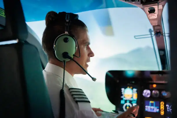 Rear view of a male pilot flying helicopter. Pilot wearing headset discussing with co-pilot during flight.