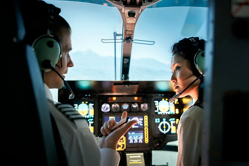 Female trainee pilot listening to instructor during a flight simulation training. Woman learning to fly helicopter with instructor inside a flight simulator.
