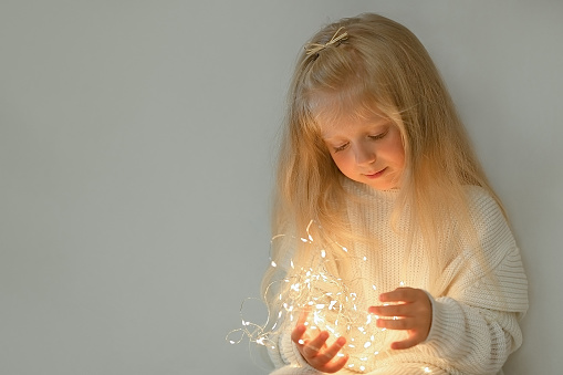 Pretty little girl looking down on the christmas lights in her hands