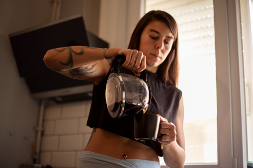 Thirty-five-year-old brunette woman is drinking coffee in the kitchen of her home. As the coffee culture spread, the kitchens of the houses became very comfortable places for experimental coffee experiences.