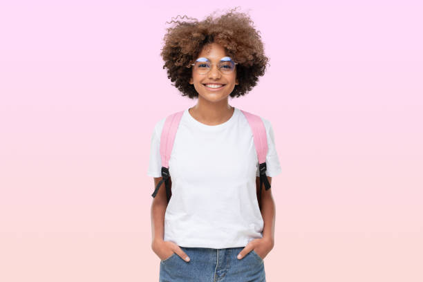 portrait d’écolière africaine souriante en t-shirt blanc, lunettes et sac à dos, isolée sur rose - schoolgirl photos et images de collection