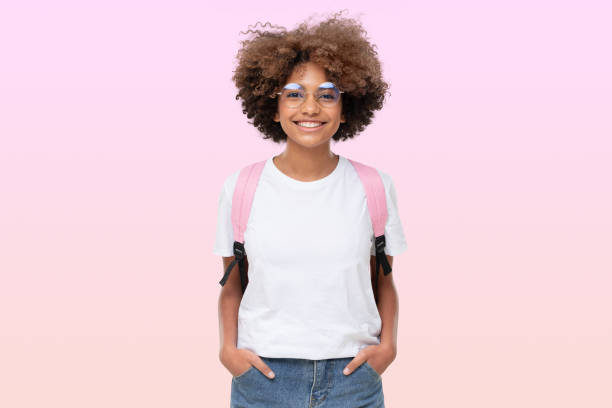 白いtシャツ、眼鏡、バックパックを着た笑顔のアフリカの女子生徒の肖像画、ピンクに隔離 - 女子生徒 ストックフォトと画像
