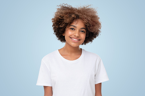 Smiling african girl in white t-shirt looking at camera, isolated on blue background