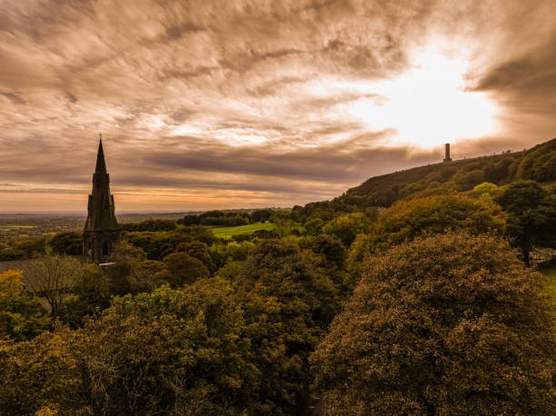 Church Steeple Drone photograph of Emanuel Church steeple rising above autumnal trees at Holcombe Brook, Ramsbottom, Bury, England hope god lighting technique tree stock pictures, royalty-free photos & images