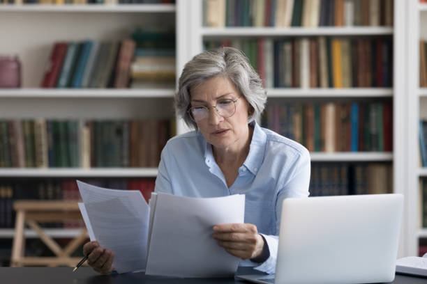 poważna, zamyślona kobieta w średnim wieku martwiła się czytaniem wiadomości w dokumencie - pensive women business mature adult zdjęcia i obrazy z banku zdjęć