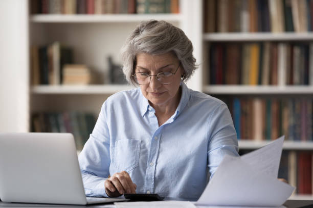 istock Older woman sits at table calculates summary for monthly payment 1435621182