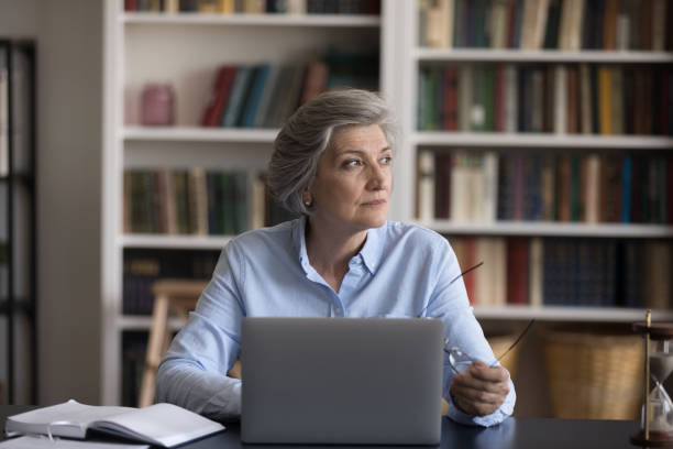 istock Older businesswoman sit at workplace distracted from work staring aside 1435621213