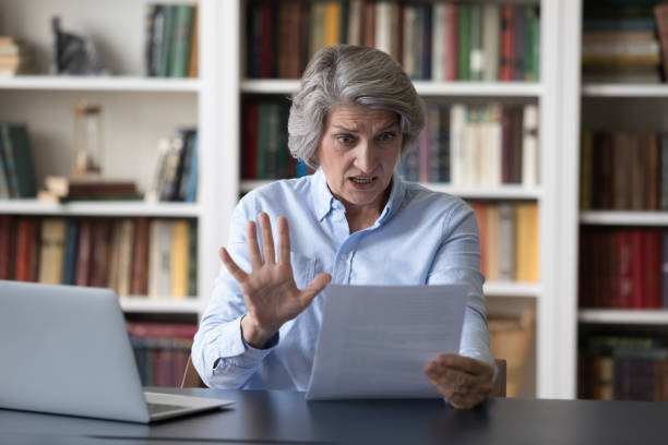 Astonished shocked older businesswoman gawp at paper letter Astonished older businesswoman sit at desk gawp at written information on paper notice feels shocked, looks stressed due unexpected awful news, bank debt, high taxes to pay, financial problems concept gawp stock pictures, royalty-free photos & images