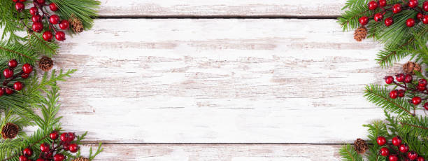 istock Winter double border with evergreen branches, red berries and pine cones on a rustic white wood banner background 1435623684