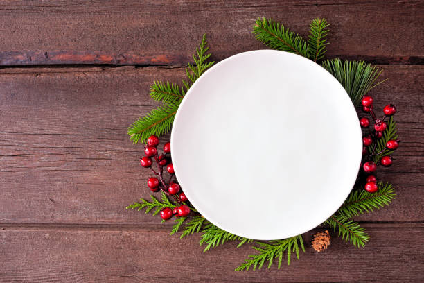 istock Christmas table setting mock up white plate with frame of evergreen branches and red berries on a dark wood background 1435623731