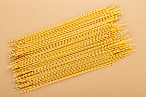 Dry spaghetti pasta on a beige background. Yellow italian pasta close-up. Top view