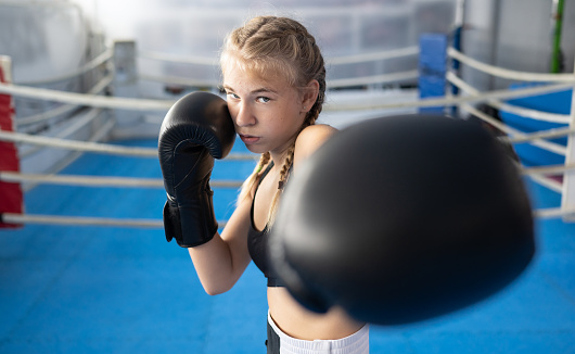 Portrait of determined teenage girl boxer in a fighting stance on sports training in a gym. Combat sport and Kids sport concept.