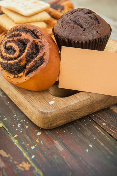 Cinnamon bun and chocolate muffin on a vintage style wooden backdrop with empty business card template