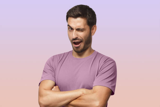 Studio shot of young man winking while flirting on purple background Studio shot of young man winking while flirting, isolated on purple background young man wink stock pictures, royalty-free photos & images
