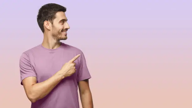 Photo of Casual dressed man in t-shirt looking right pointing with his finger, isolated on purple background