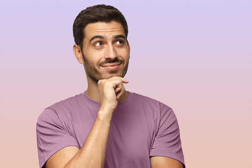 Portrait of young man in purple t-shirt with dreamy cheerful expression, thinking, isolated on purple background with copy space for your ads