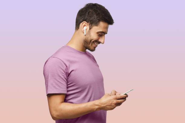 side portrait of handsome man in purple tshirt, looking at screen of smartphone surfing internet - city life audio imagens e fotografias de stock