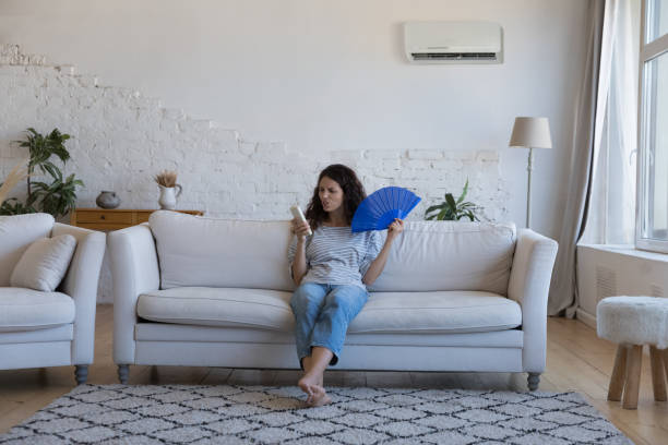 istock Annoyed woman holding fan and remote controller from broken airconditioner 1435630981