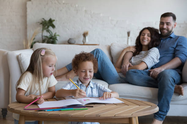 istock Preschoolers siblings drawing with pencils, parents resting on sofa 1435631331