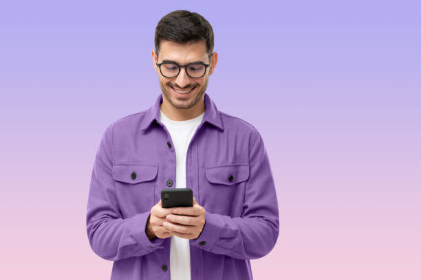 istock Young man looking at phone, standing on purple background 1435632761