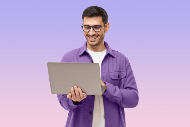 Happy man standing with opened laptop, browsing online or typing message, isolated on purple