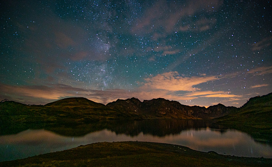 milky way and stars on a cloudy night above the lake with a reflection and colourful clouds
