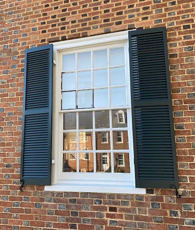 Historic Buildings of Fairfax Virginia reflecting in a window of it’s Historic Courthouse built in 1799. Window with white square panes, black wooden shutters, brick building surround.