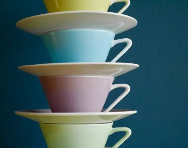 Photo of Close up of stacked pastel vintage coffee cups against petrol background.