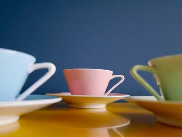 Photo of Row of vintage pastel tea cups on yellow table against petrol background. Afternoon tea party.