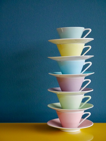 Stack of pastel vintage coffee cups on yellow table against petrol background. Vertical.