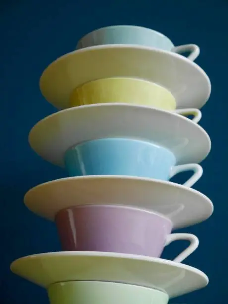 Photo of Close up of stacked pastel vintage coffee cups against petrol background.